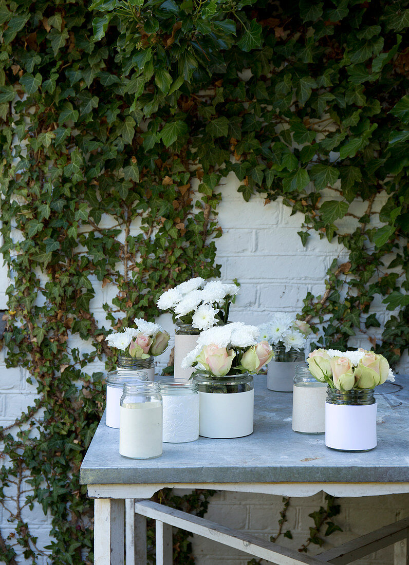 Schraubgläsern mit Manschetten aus Papier mit weißen Rosen und Chrysanthemen