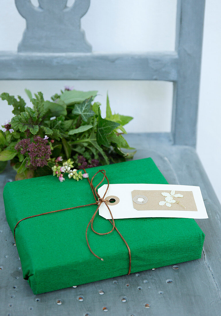 Gift wrapped in green paper with a tag and a bouquet from the garden