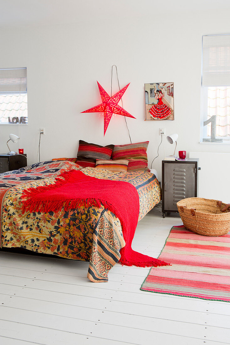 Doppelbett mit bunter Tagesdecke und roter Fransentuch, rote, sternförmige Lampe an der Wand