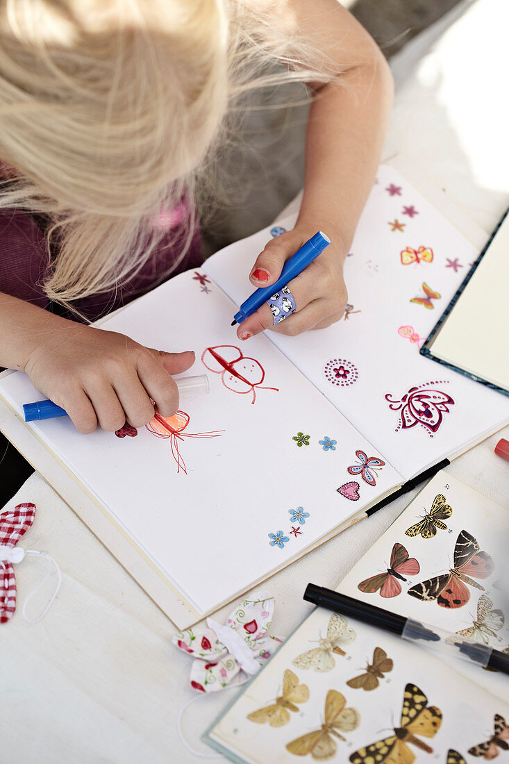 Mädchen malt Schmetterlinge in ein Notizbuch