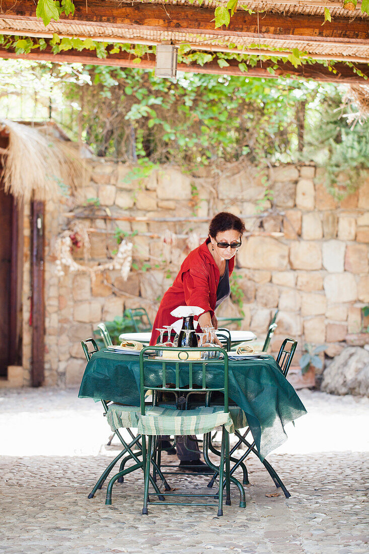 Frau mit Sonnenbrille deckt den Tisch auf mediterraner Terrasse