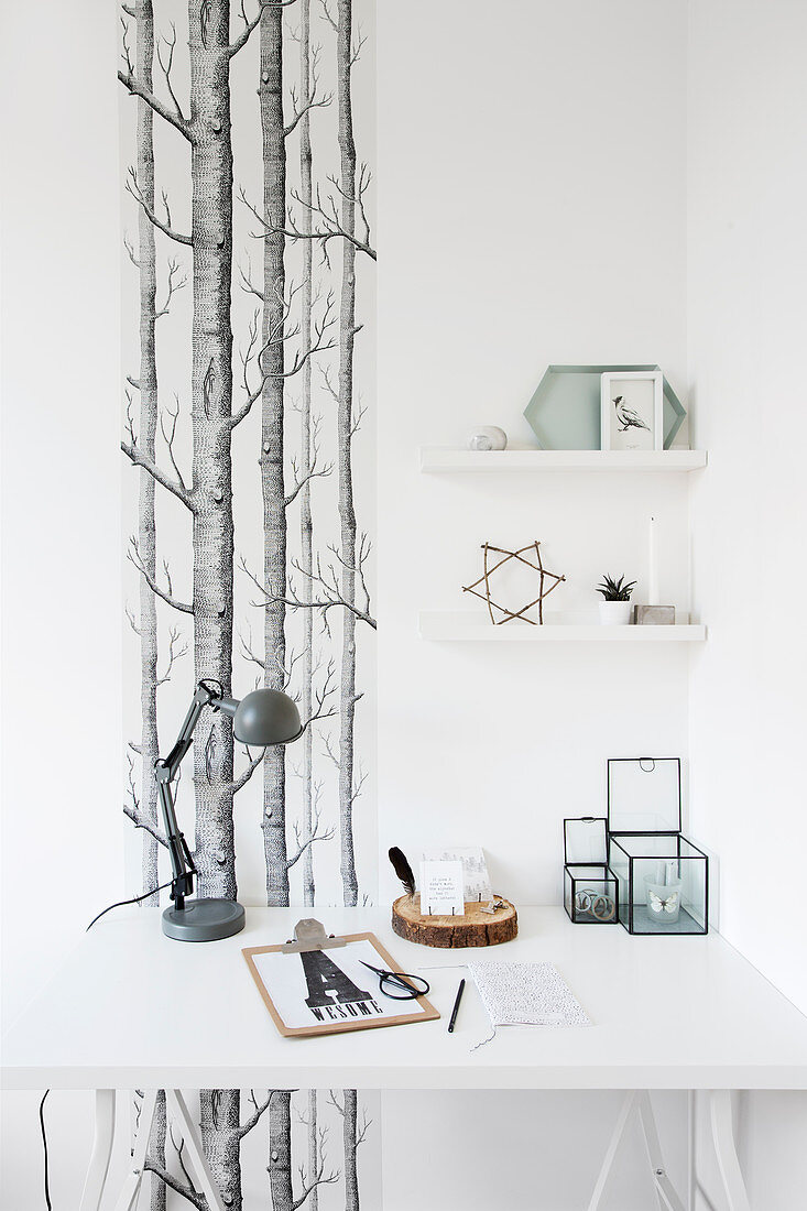 White desk with simple decoration in front of a strip of wallpaper with a forest motif