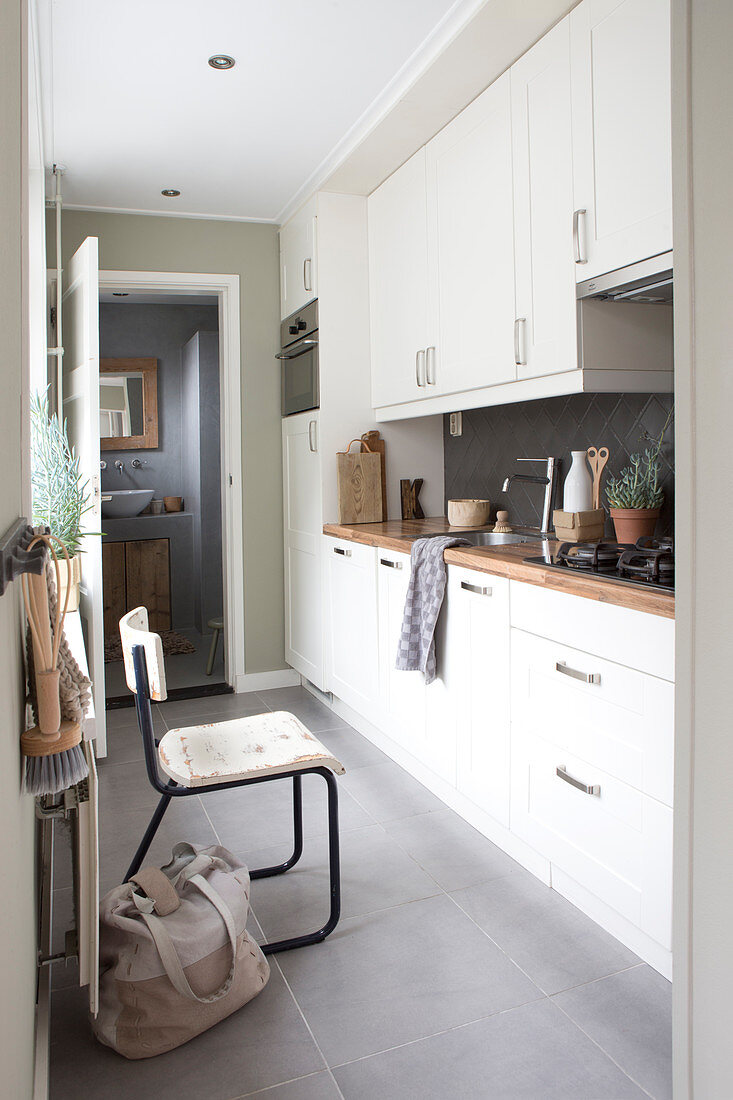 Schmale Küche mit weißer Küchenzeile und Naturdeko, Blick ins Bad
