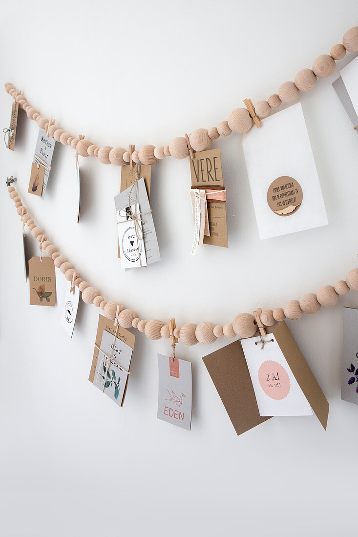 Girlande aus Holzperlenkette mit Postkarten hängen an weißer Wand