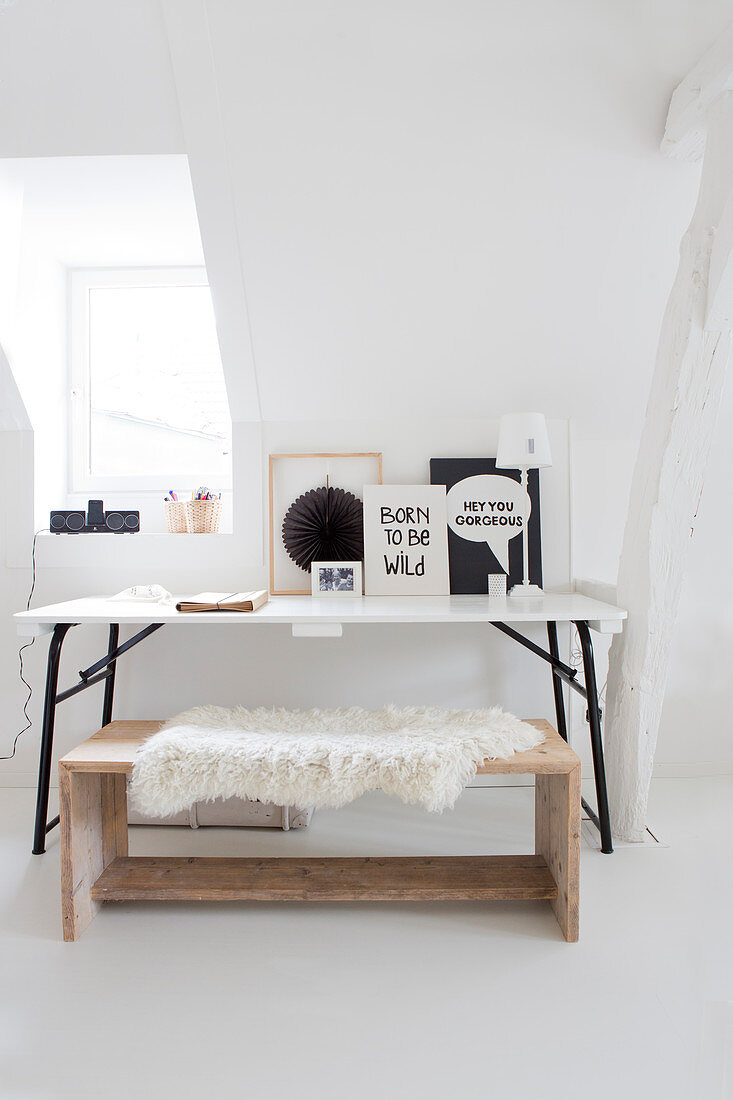 A work corner with a white table, black-and-white decorations and a wooden bench covered with an animal fur