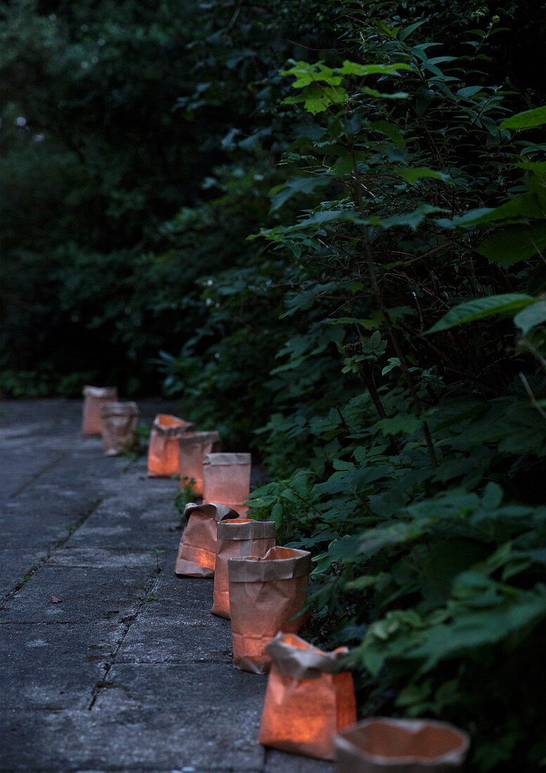 Lanterns in brown paper bags on the path in the evening summer garden