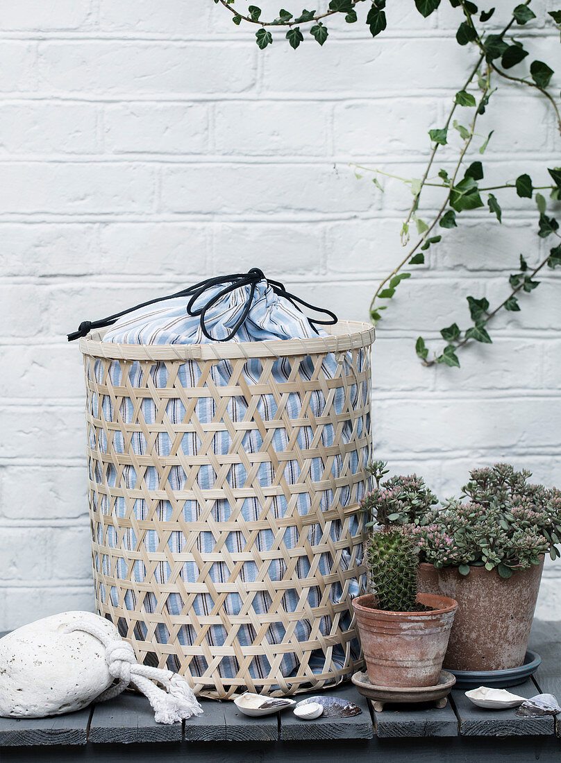 Laundry basket with a striped fabric sack in front of a white brick wall