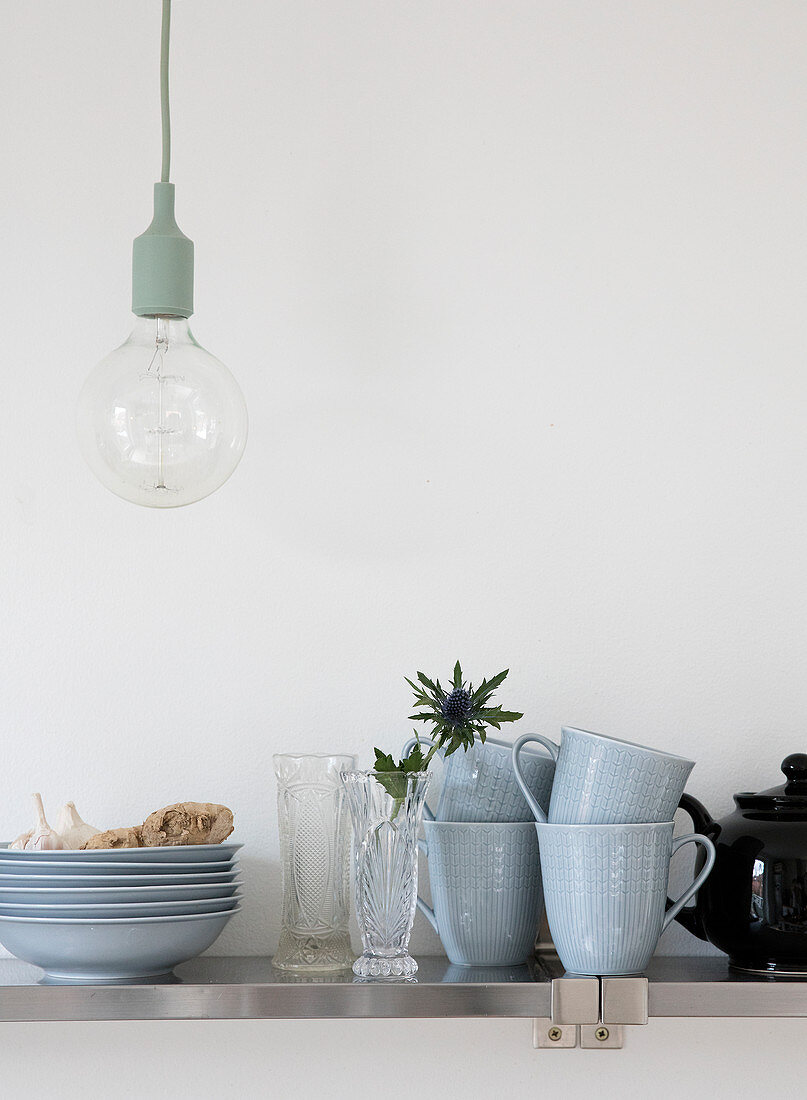 Light blue dishes, vases, and thistles on the kitchen shelf under the pendant light