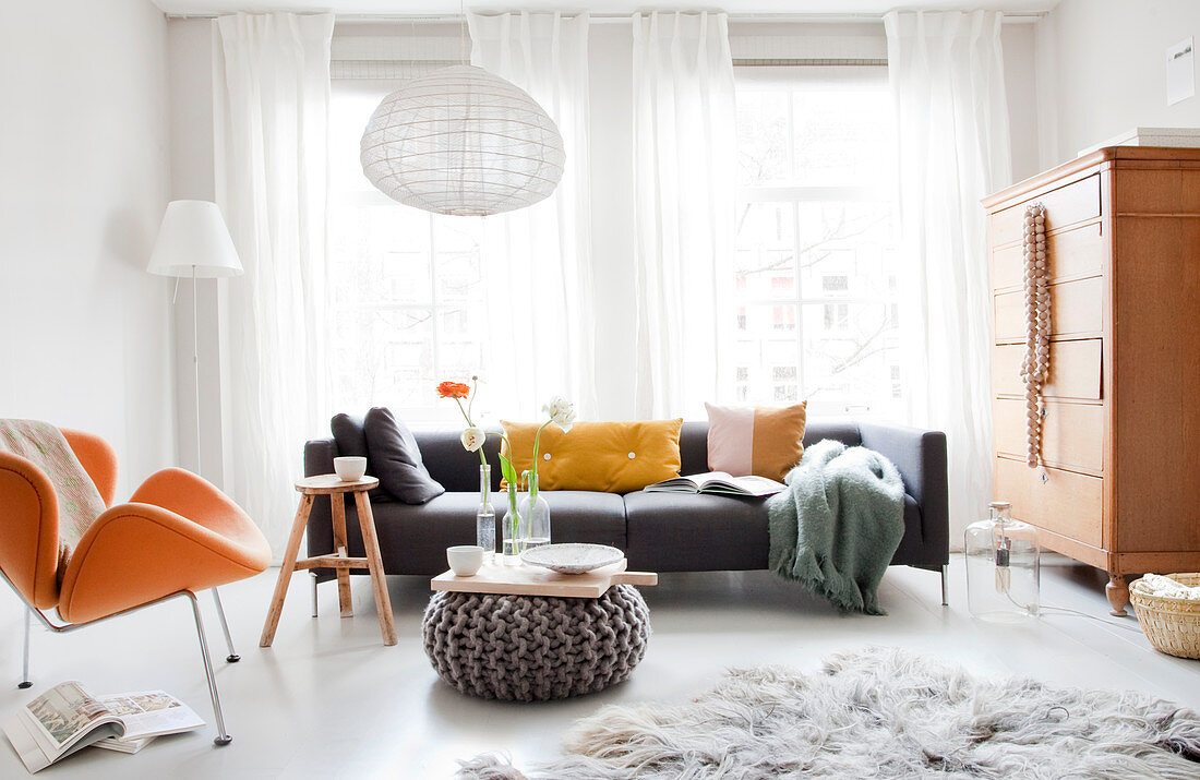Helles Wohnzimmer mit Designersessel, Sofa und Strickpouf als Cochtisch
