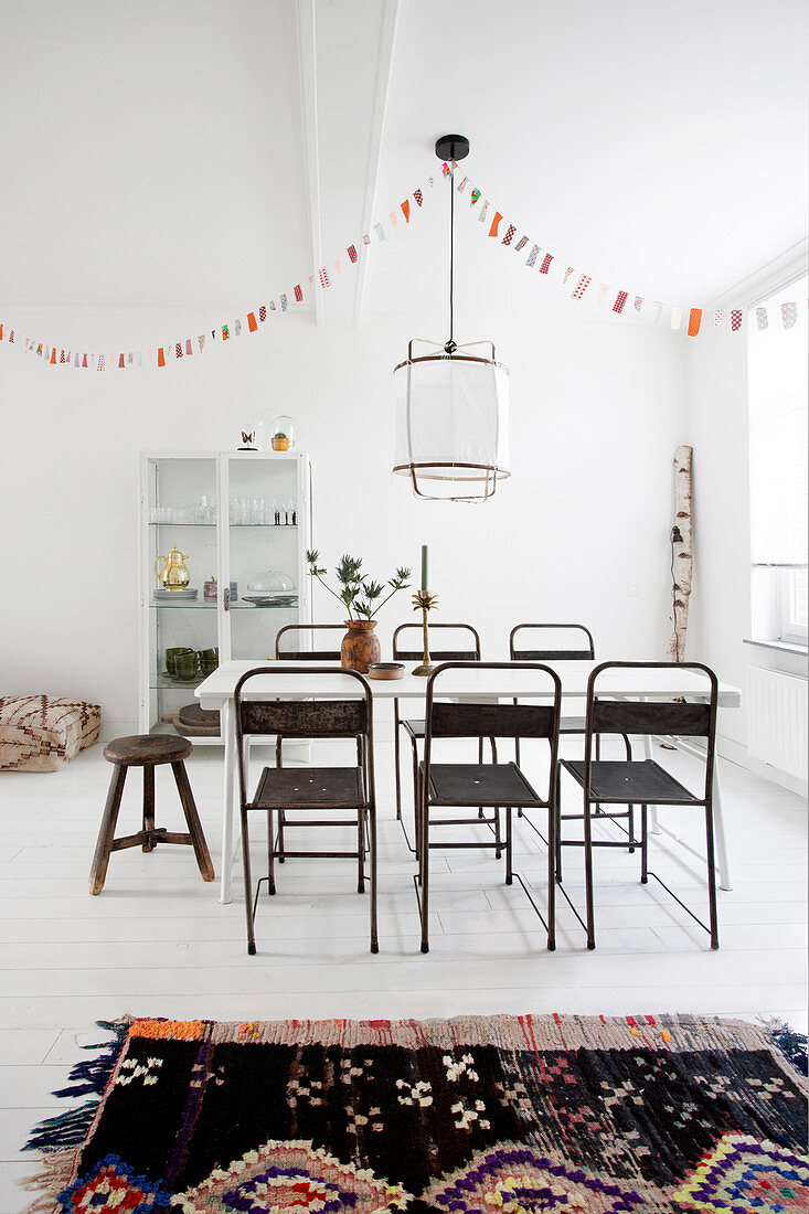 Old metal chairs at a table under a garland in a dining room with a white floor