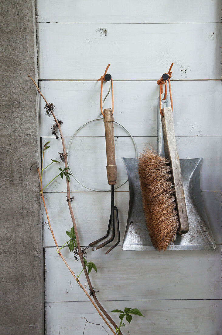 Garden tools and a dustpan and brush hanging on a wooden wall