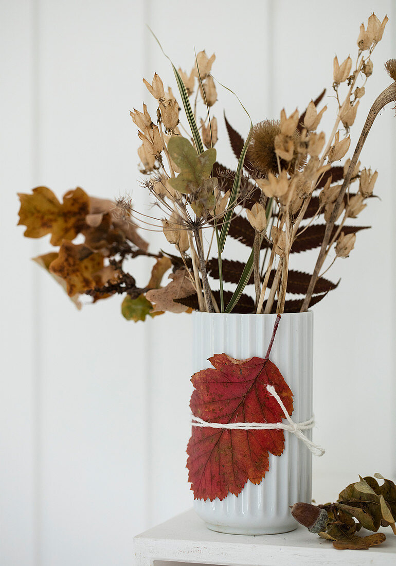 Getrocknete Blumen und Zweige in Vase mit Herbstblatt dekoriert