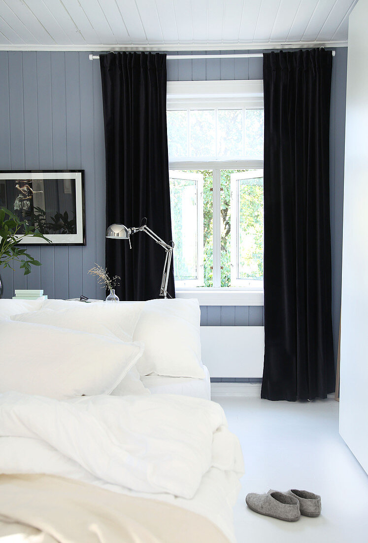 Doppelbett und schwarze Vorhänge in blau-grauem Schlafzimmer