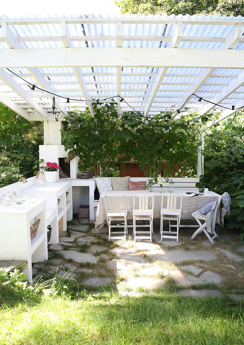 Esstisch mit Stühlen und Bank und Grünpflanzen auf überdachter Terrasse