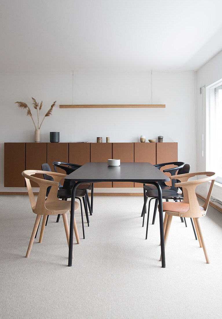 A black dining table with chairs in front of a brown sideboard