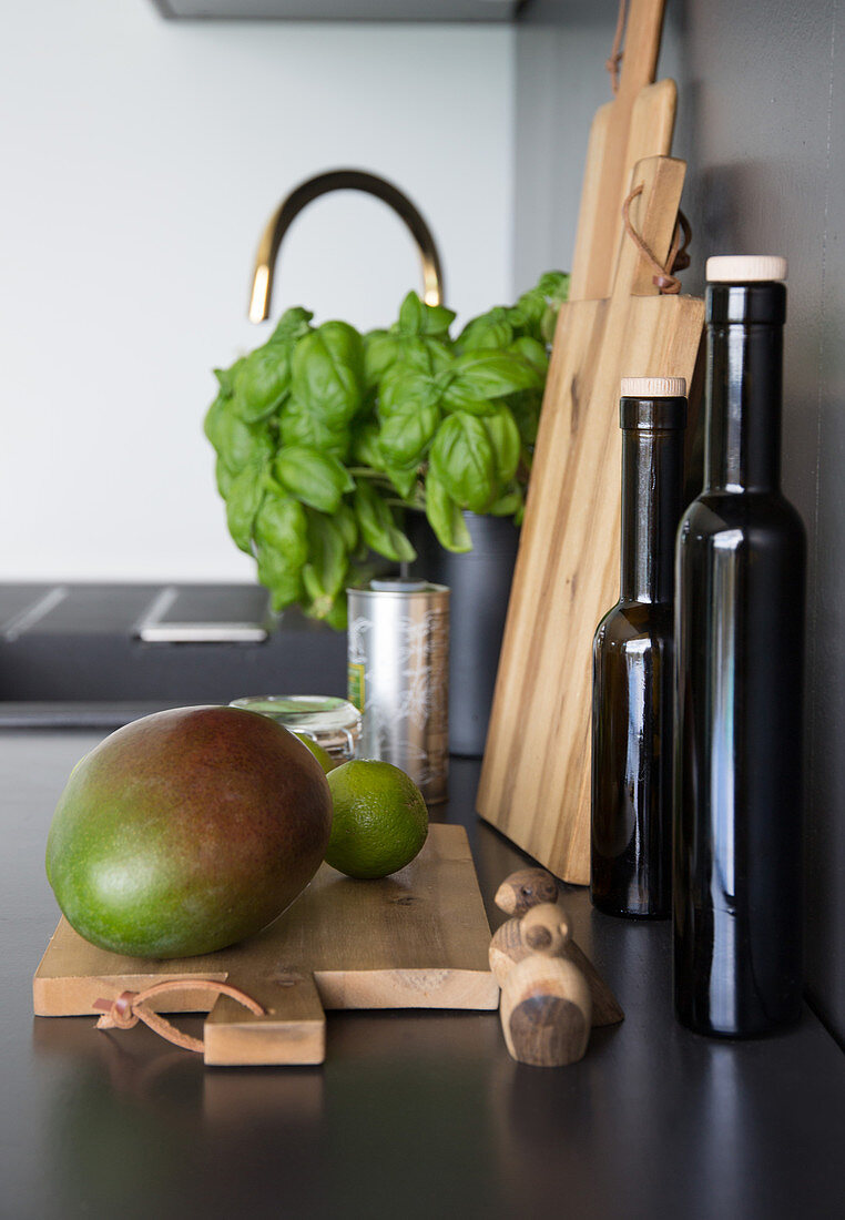 A mango on a wooden board with oil bottles and basil on a kitchen worktop