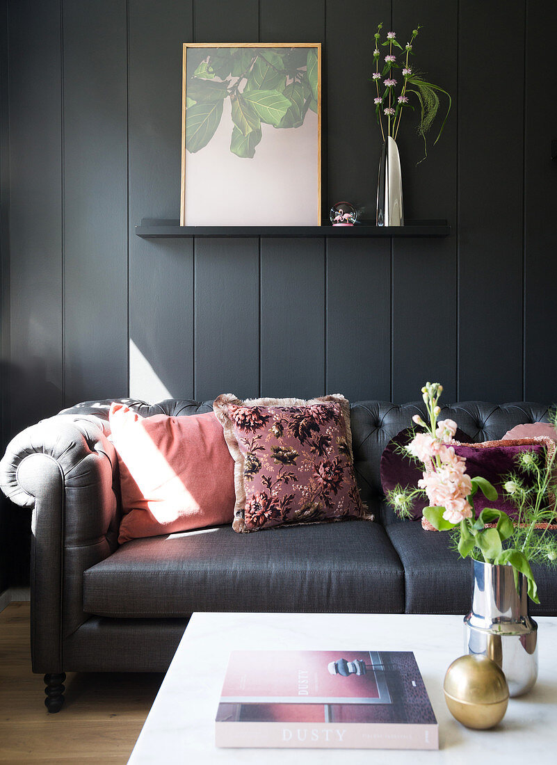 A dark sofa with pink cushions in front of a dark wall