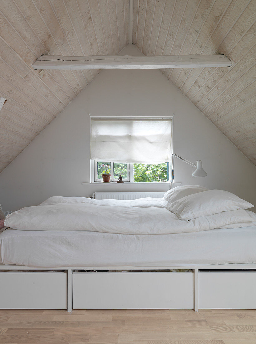 A bed with drawers in a small bedroom under the roof