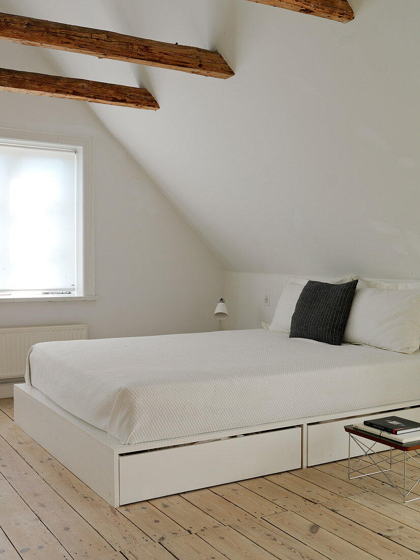 A bed with drawers in a simple bedroom under the roof