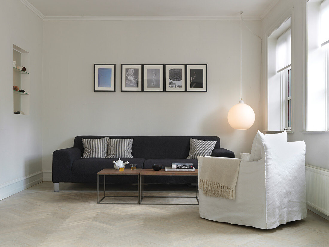 Weißer Sessel vorm schwarzen Sofa im minimalistischen Wohnzimmer