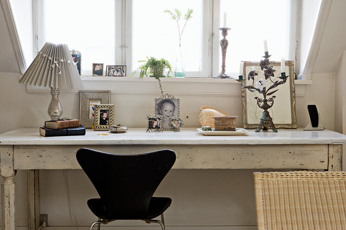Designerstuhl am alten weißen Schreibtisch mit Fotos unterm Dachfenster