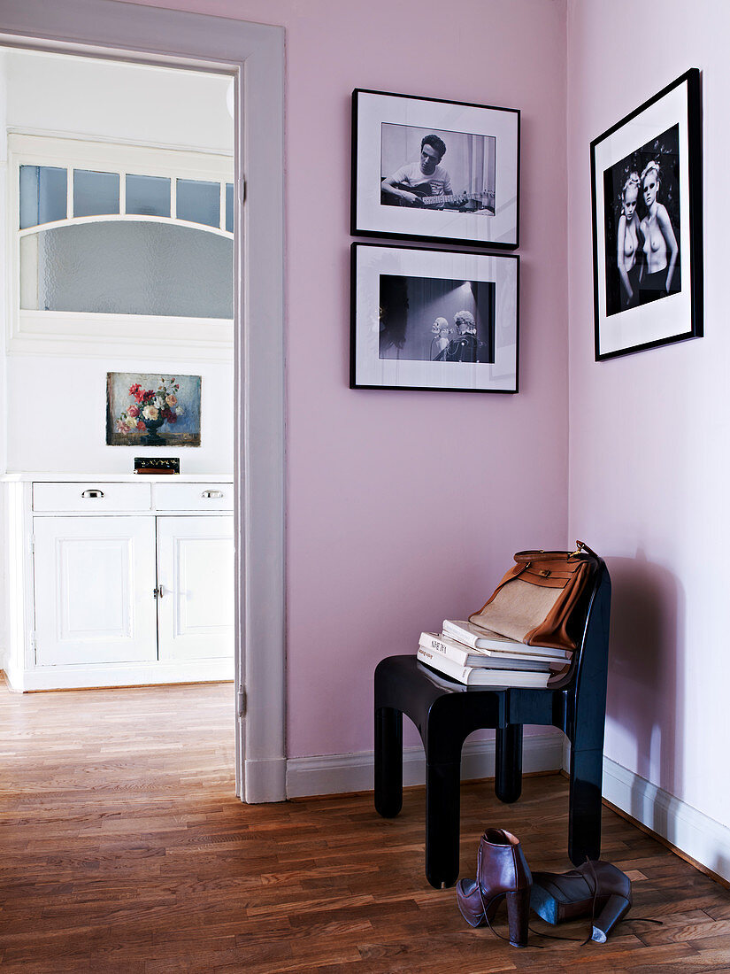 Schwarzer Stuhl vor rosafarbener Wand mit Schwarz-Weiß-Fotos im Flur