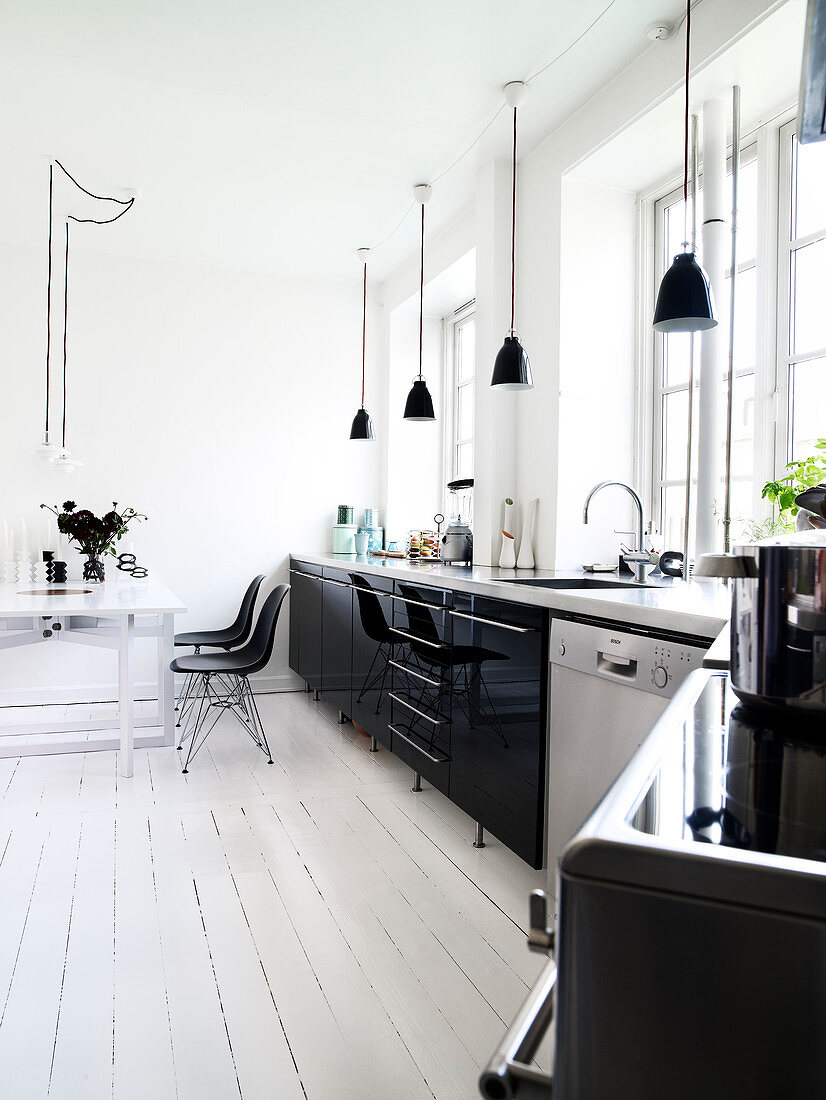Black high-gloss kitchen and dining area in an old apartment with white plank floor