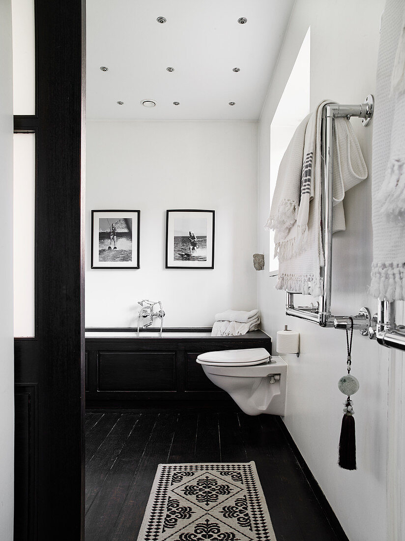 Toilette und Badewanne im Badezimmer mit weißen Wänden und schwarz lackiertem Dielenboden