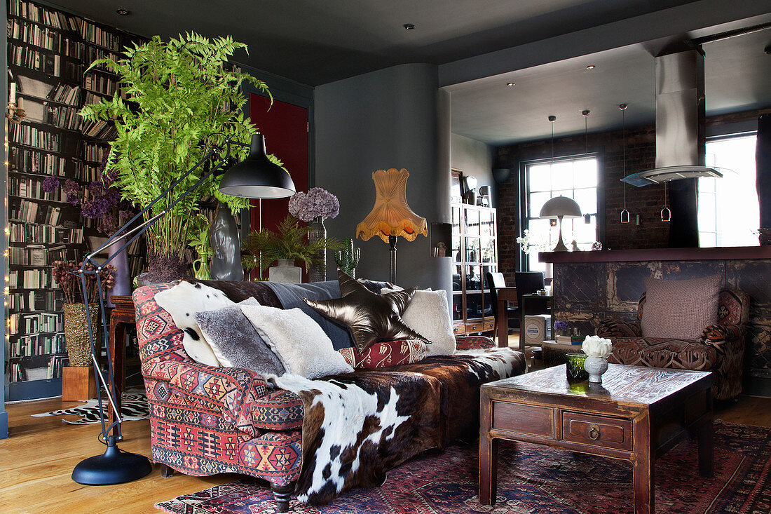 Kissen und Tierfell auf Sofa mit Ethno-Bezug, dahinter Konsolentisch mit Zimmerpflanze im Wohnzimmer