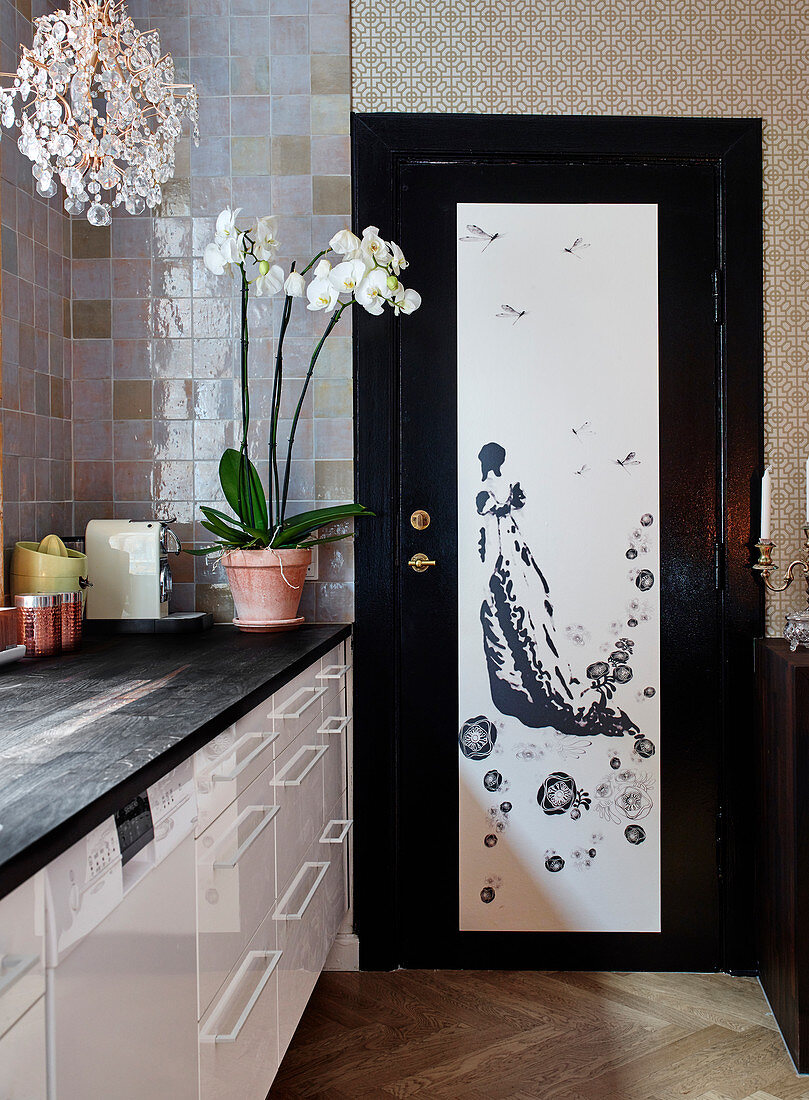 Weiße Küchenzeile mit schwarzer Arbeitsplatte, Orchidee und Kronleuchter, Tür mit asiatischem Motiv