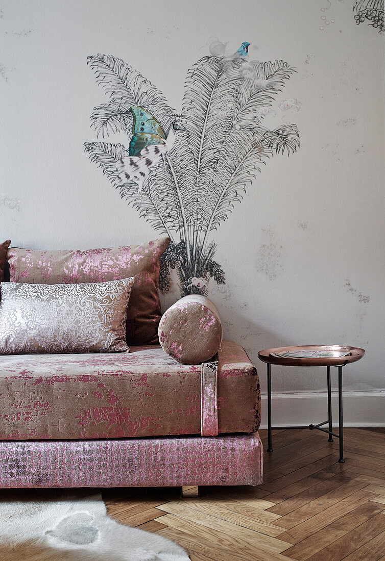An elegant sofa and a side table in front of a wall papered with palm tree wallpaper
