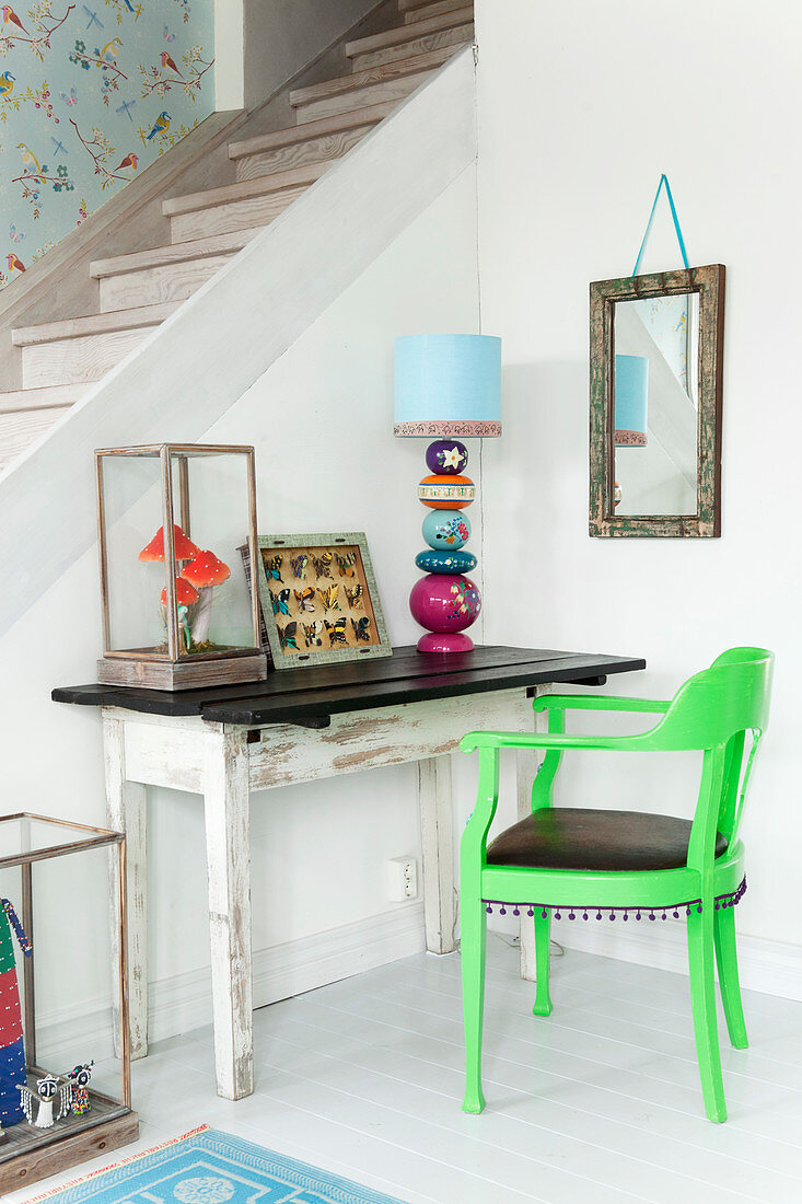 Alter Holztisch mit Tischlampe und grüner Armlehnstuhl vor Treppenwand in Zimmerecke