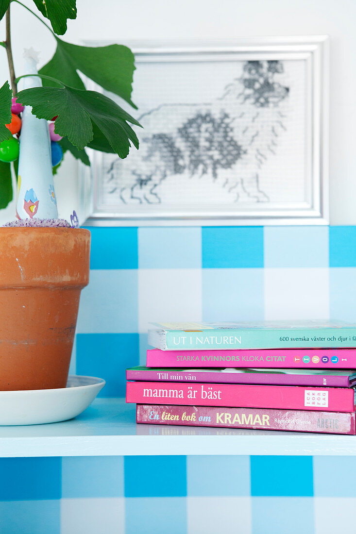 Zimmerpflanze und Bücher auf Wandregal mit blau-weiß karierter Rückwand