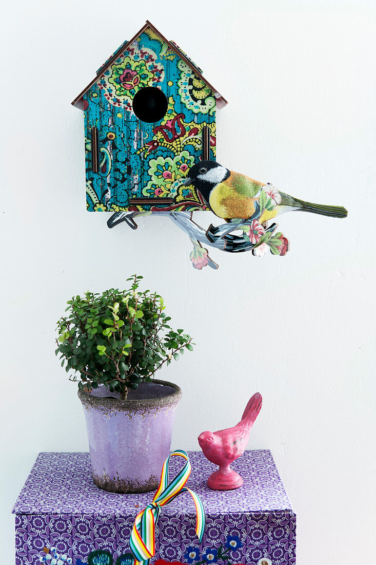 Vogelhäuschen und Dekovogel an der Wand, darunter Topfpflanze