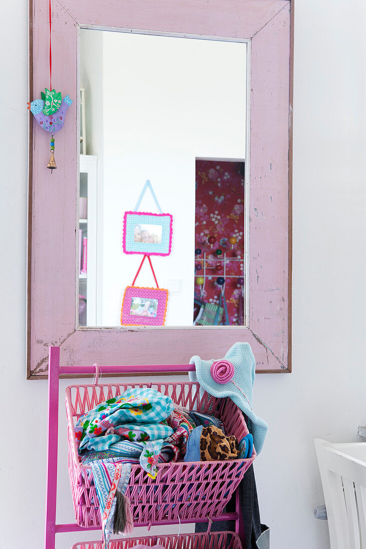 Pink basket with towels in front of wall mirror with pink painted wooden frame