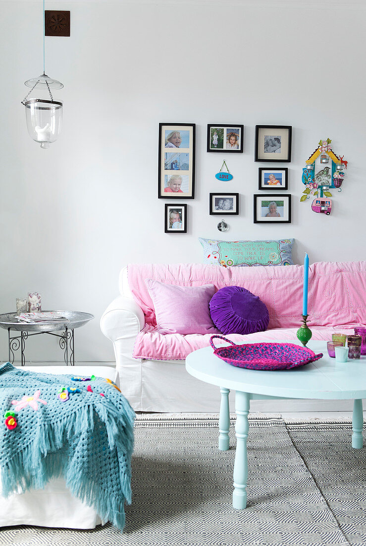 Sofa mit weißer Husse und rosa Kissen im Wohnzimmer, im Vordergrund runder Tisch und Sitzwürfel mit Häkeldecke