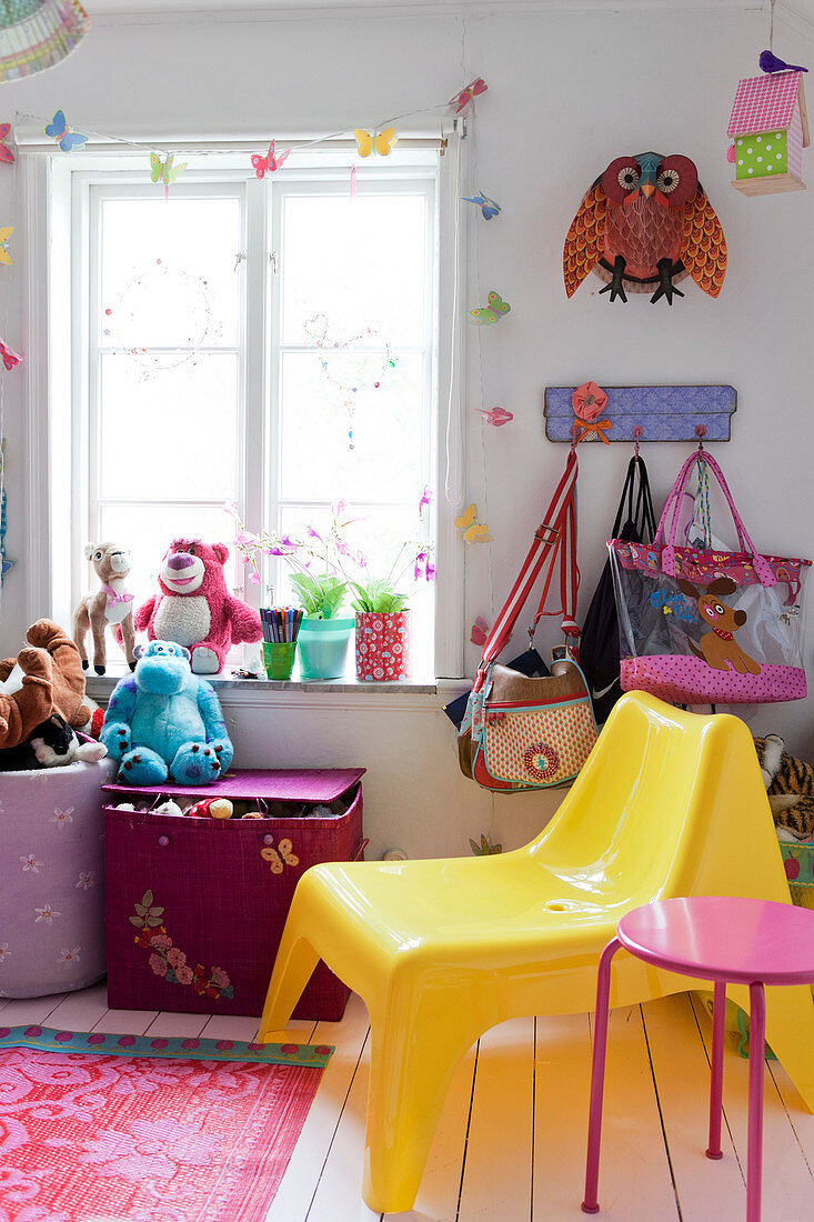 Gelber Kunststoff-Stuhl, Taschen und Stofftiere am Fenster im Kinderzimmer