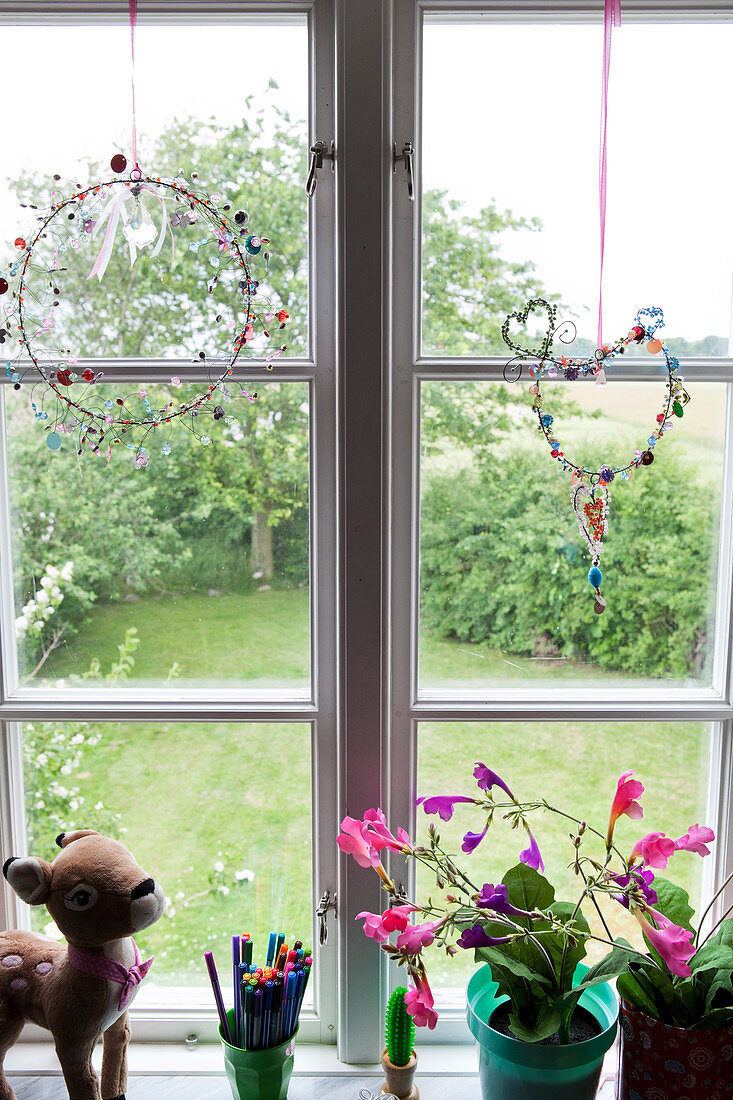 Fensterdekoration mit Perlen, Zimmerblumen, Stiftehalter und Plüsch-Bambi auf Fensterbank