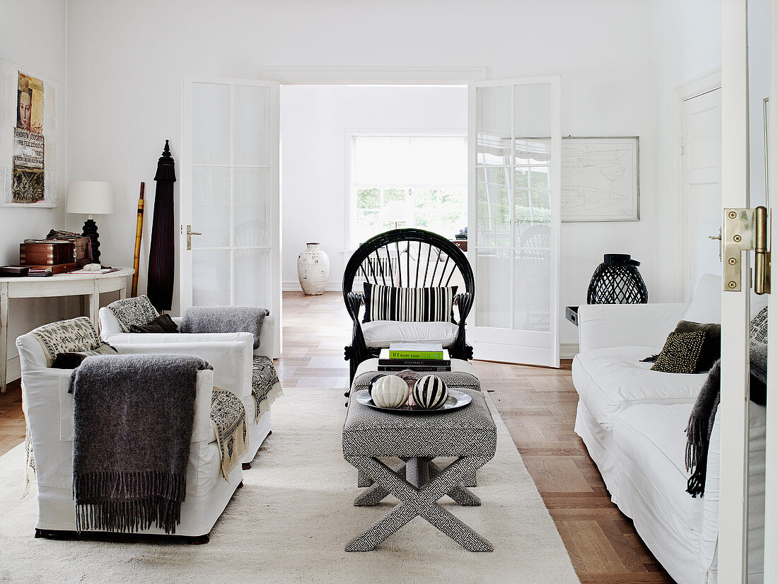 Weiße Hussenmöbel, gepolsterte Hocker als Couchtisch und Rattanstuhl im Wohnzimmer