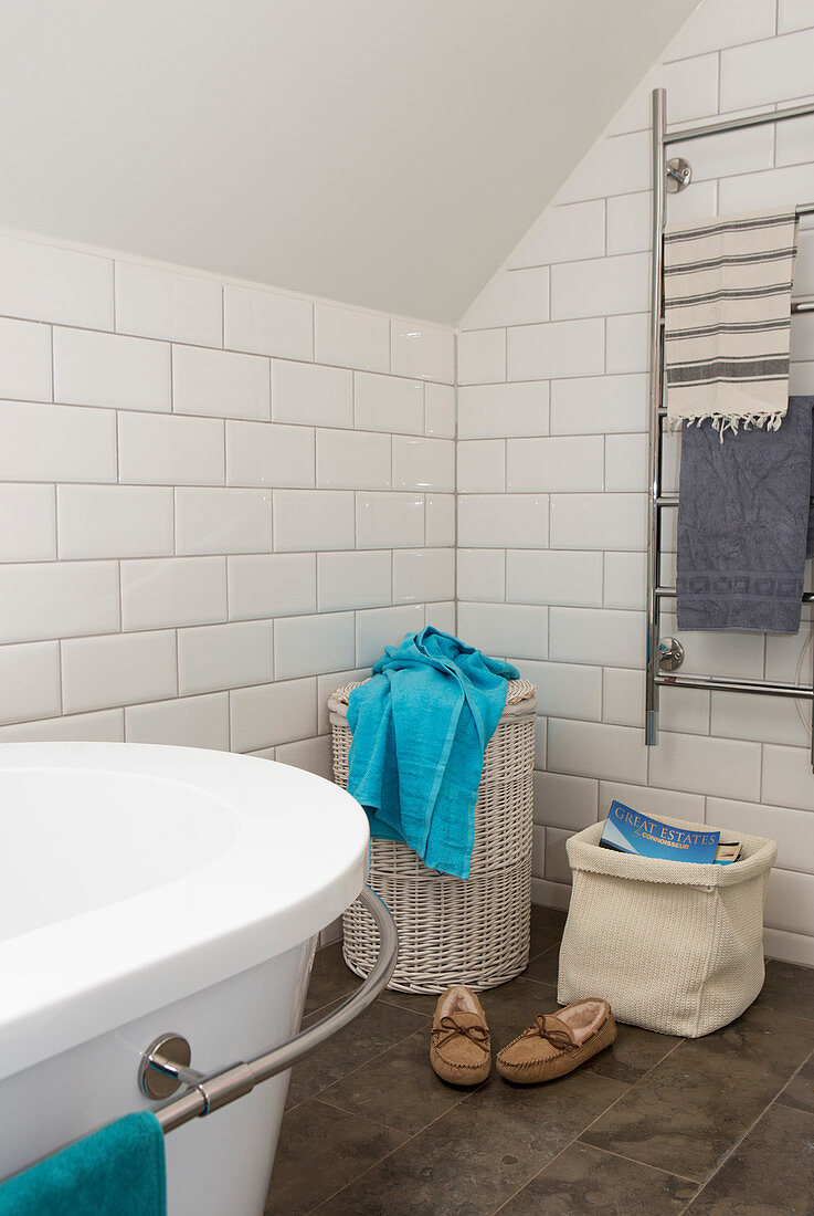 Laundry basket, magazine basket, and towel dryer in a bathroom with white subway tiles, bathtub in foreground