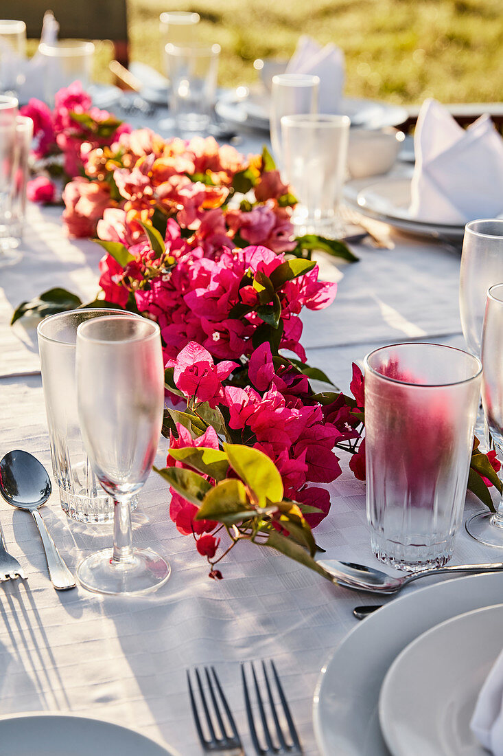 Gedeckter Tisch im Freien dekoriert mit Bougainvillea-Blütengirlande