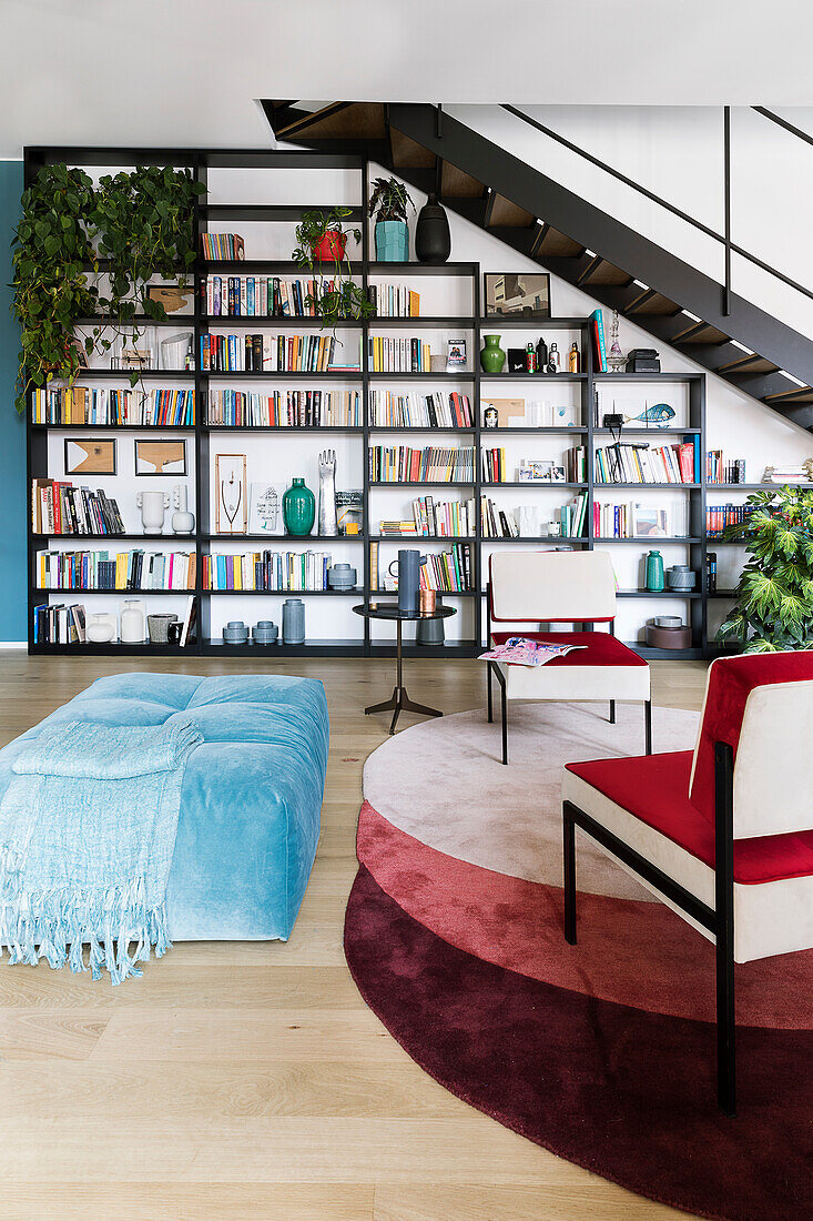 Blue and red upholstered furniture in front of bookcase below staircase