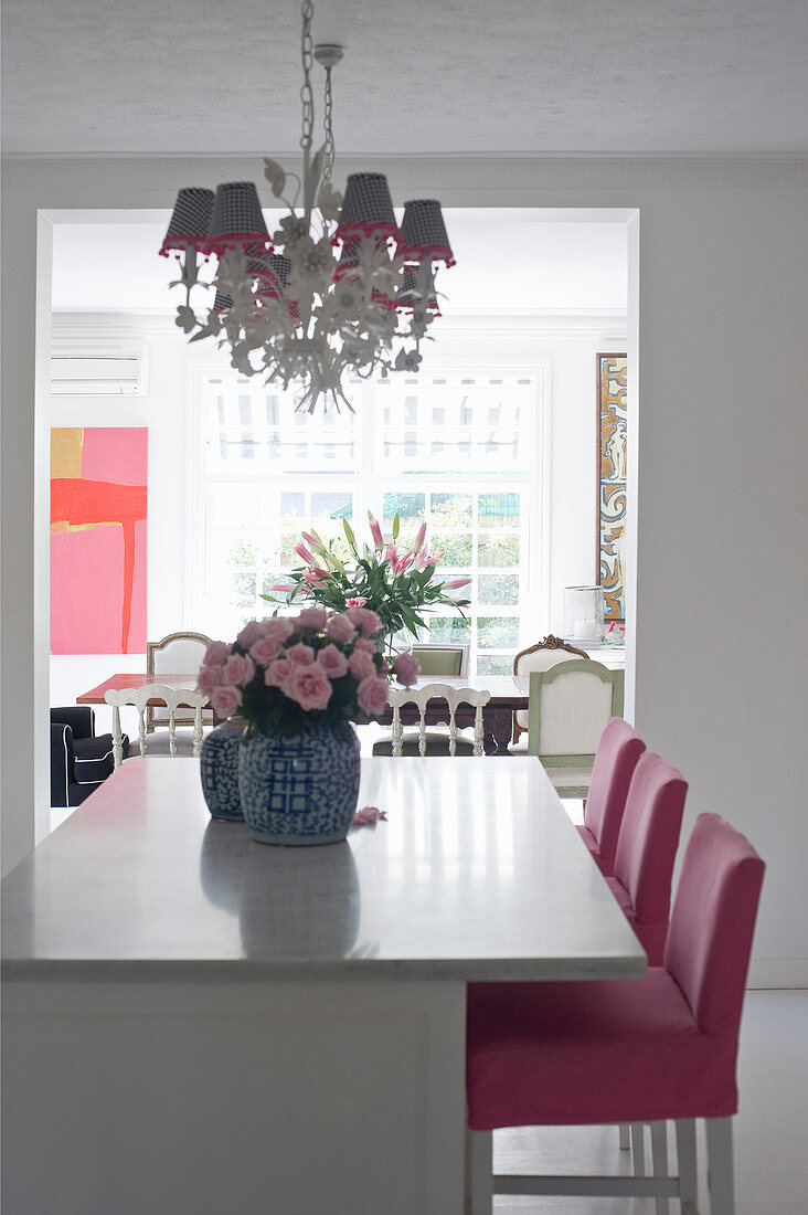 Pink bezogene Barhocker an Küchentheke, Rosenstrauß in chinesischer Vase, Kronleuchter mit Lampenschirmchen