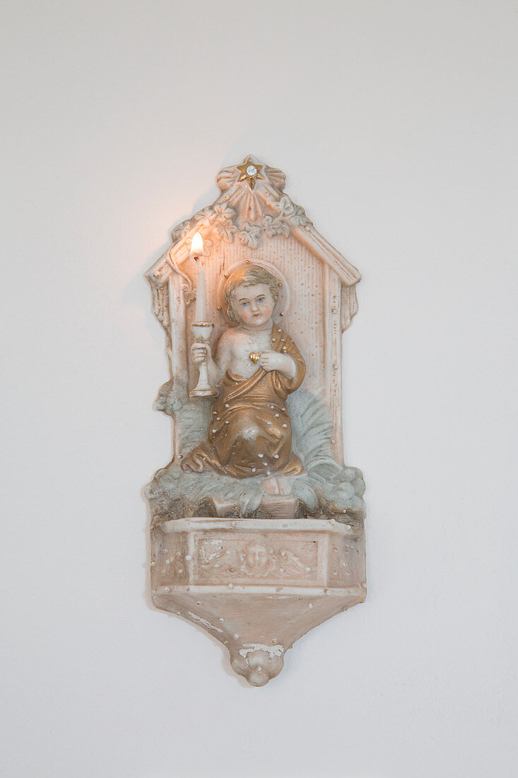 Antique sconce with angel and lit candle on wall