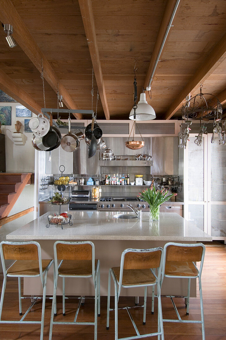 Barstools at island counter in open-plan kitchen with wood-beamed ceiling