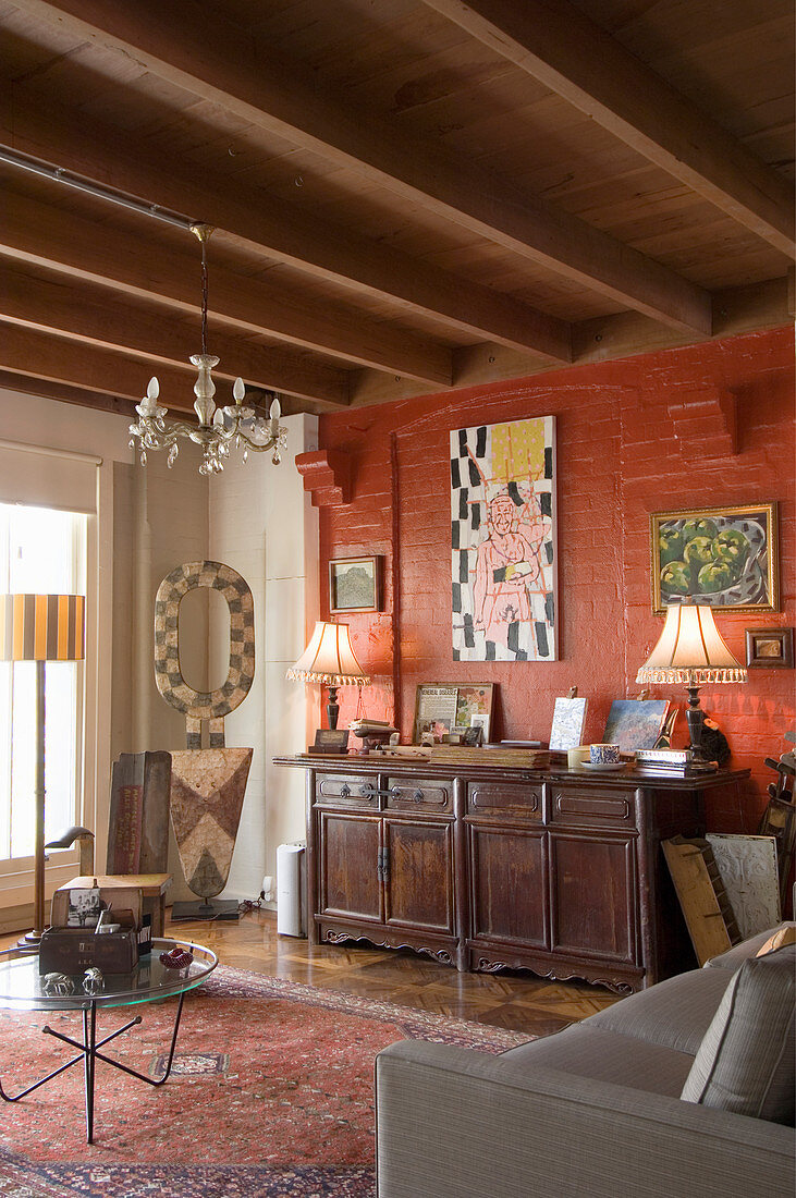 Alte Kommode vor rostroter Wand im rustikalen Wohnzimmer