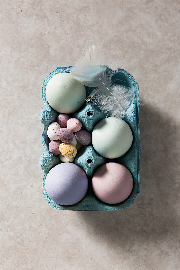 Mit Naturfarben gefärbte Eier, bunte Schokoladeneier und Feder in blauem Eierkarton