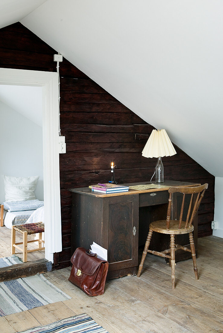 Alter Schreibtisch vor einer rustikalen Holzwand unter dem Dach