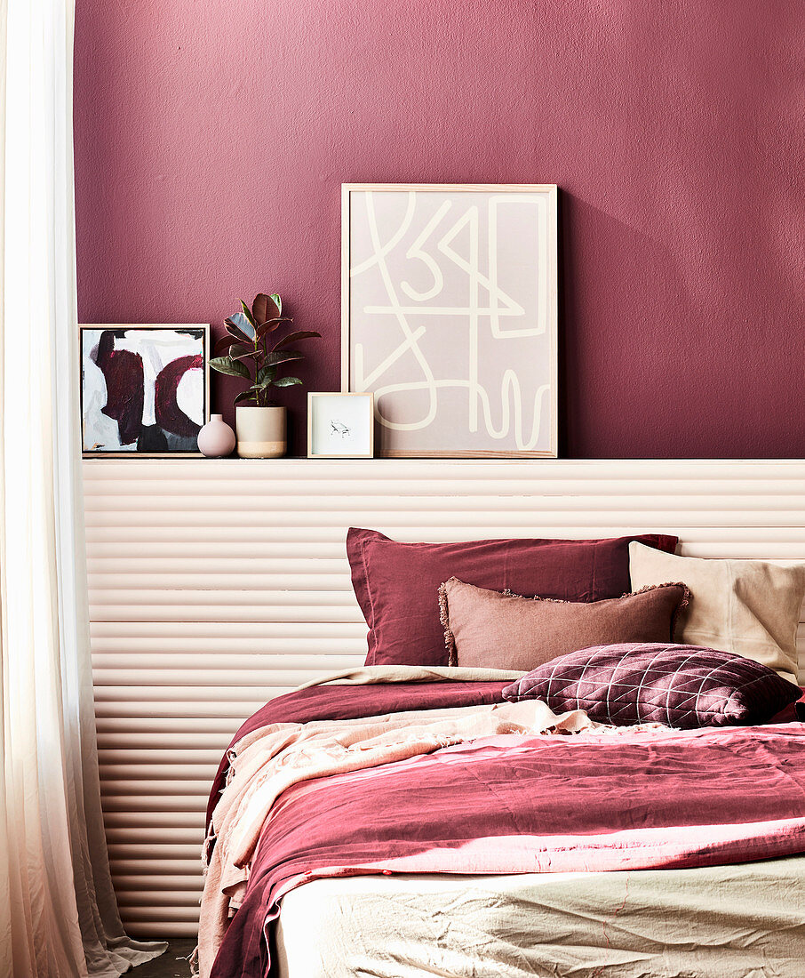 Double bed in front of the ledge with decorative objects in the bedroom, dark red wall and matching accessories