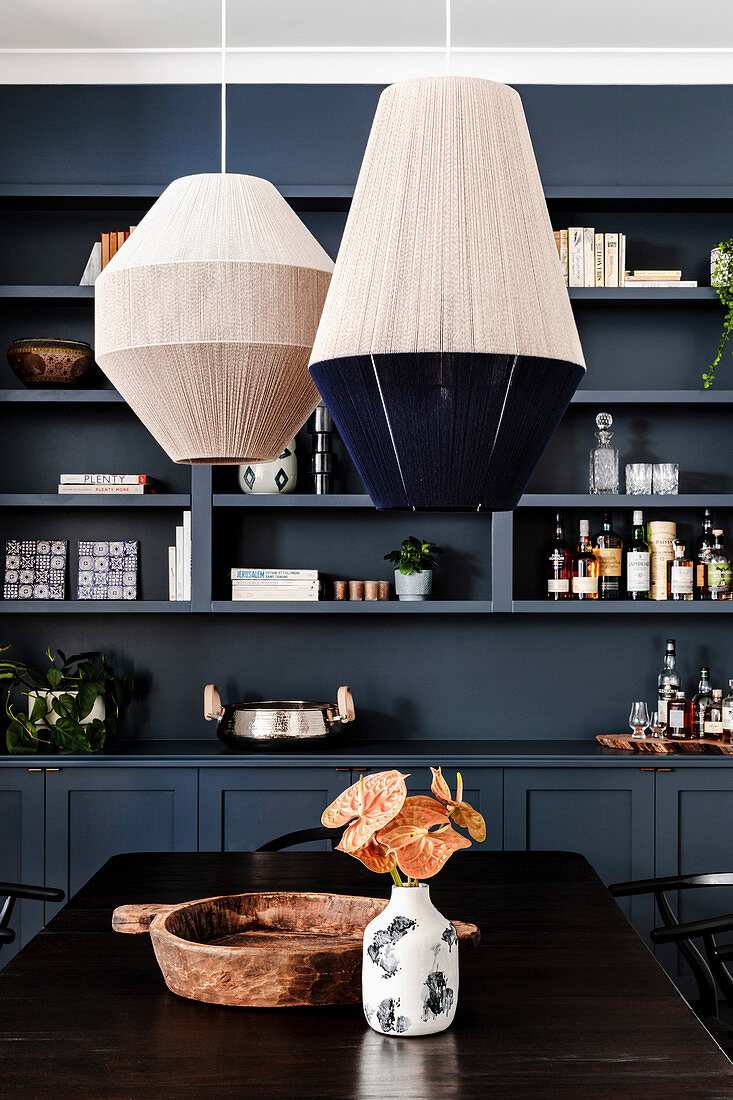 Threaded lampshades above the dining table in front of the shelf wall